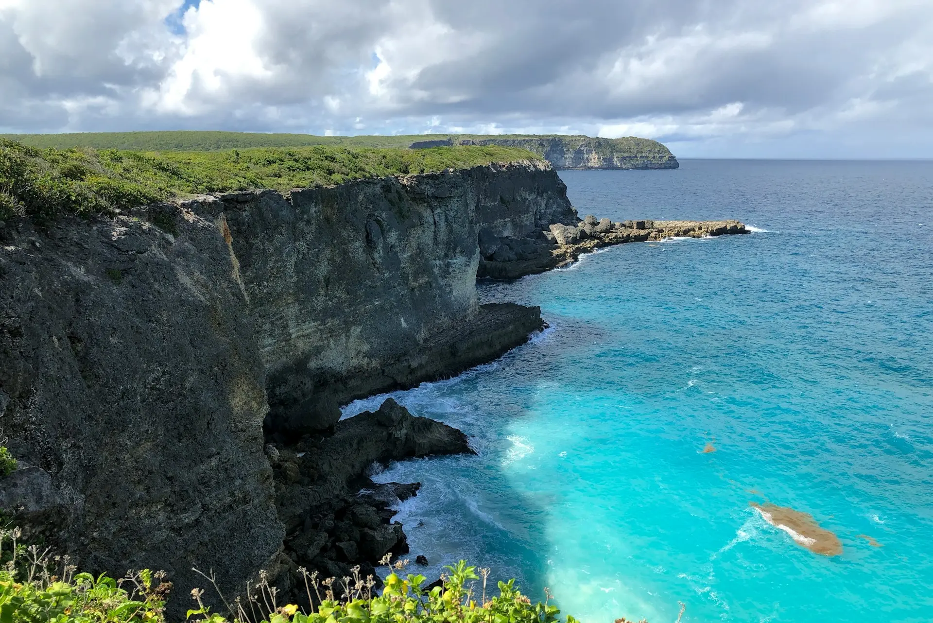 green and brown rocky mountain beside blue sea under blue and white cloudy sky during daytime